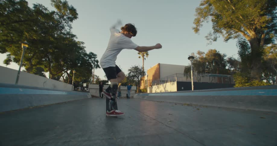 Skateboarders standing in park watch as another skateboarder with a prosthetic brace performs a trick