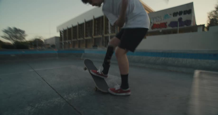 Young man attempting skateboard tricks near a building at dusk