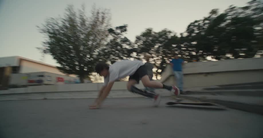 A teenage boy skateboards down some steps on a city sidewalk and falls off as two other teens watch him