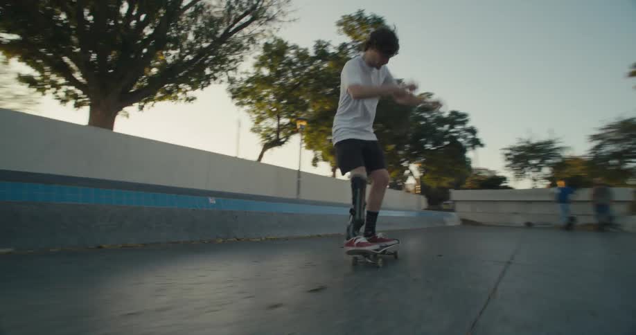 Male skateboarder with prosthetic brace flips skateboard as he rides at park