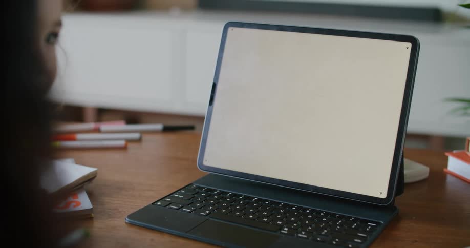 Woman with wavy hair and toddler girl looks at tablet with tablet keyboard on coffee table in living room at home