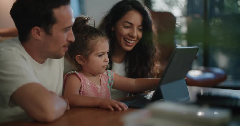 A family sit together at a kitchen table while the daughter touches the screen of a computer
