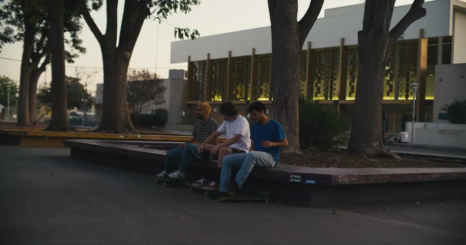 Three young men with skateboards hang out on a curb together