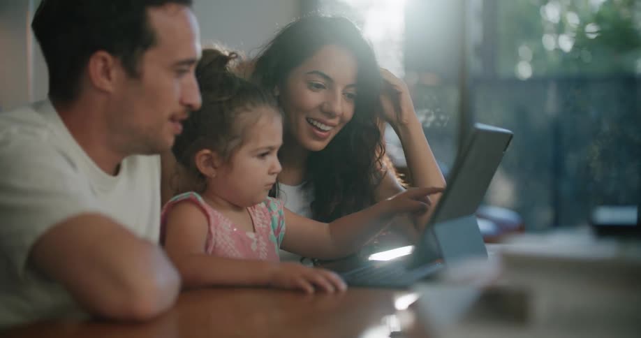 Parents and daughter smile while looking at computer in living room