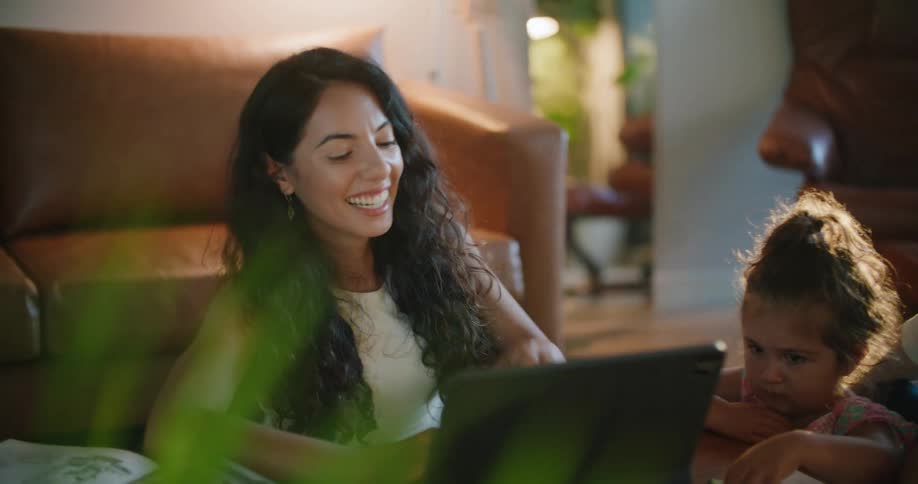 A woman laughs as she looks at her laptop and then looks at her daughter and husband as they all sit at a coffee table