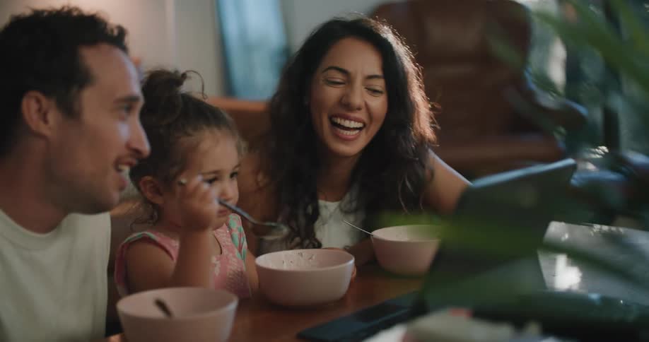 Young family eating cereal an laughing watching movie on laptop