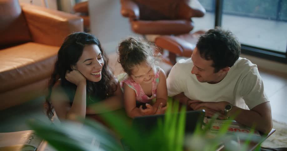 A girl kisses her father on the cheek while using a laptop with her parents