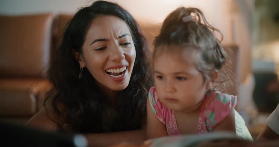 Mother with wavy hair and father with white t shirt reading magazine while daughter looking at tablet sitting at coffee table in living room at home