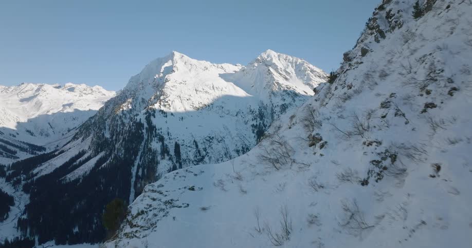 Forest sits in shadow on snowy mountain sides under a clear sky