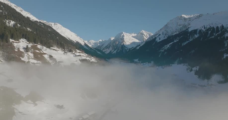 Dense fog shrouds the valley below snow covered mountains