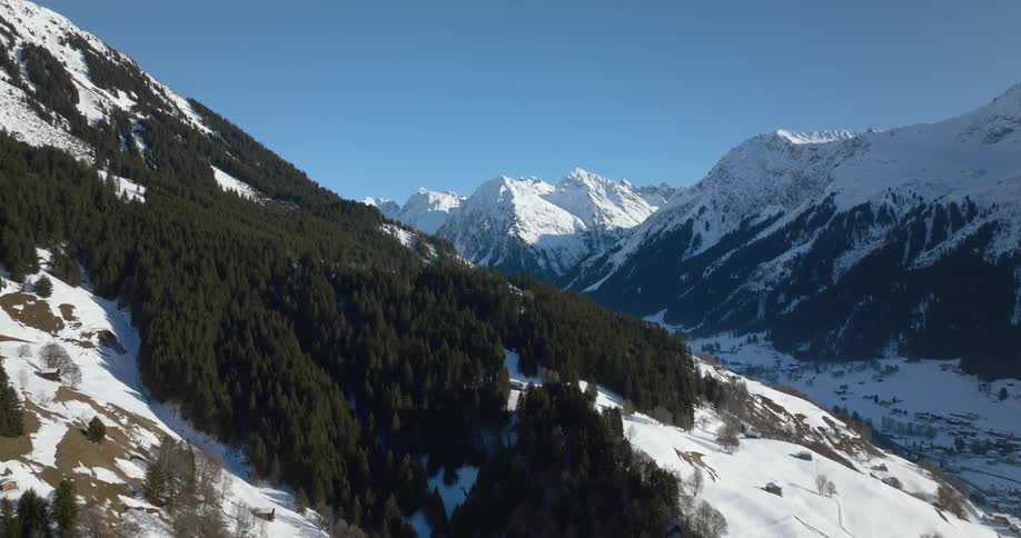 A snow covered mountain slope with cabins and homes above the valley