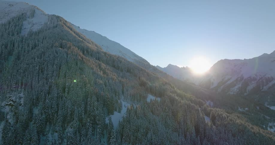 Sun shines through mountain pass on to forest and snow covered valley and mountains