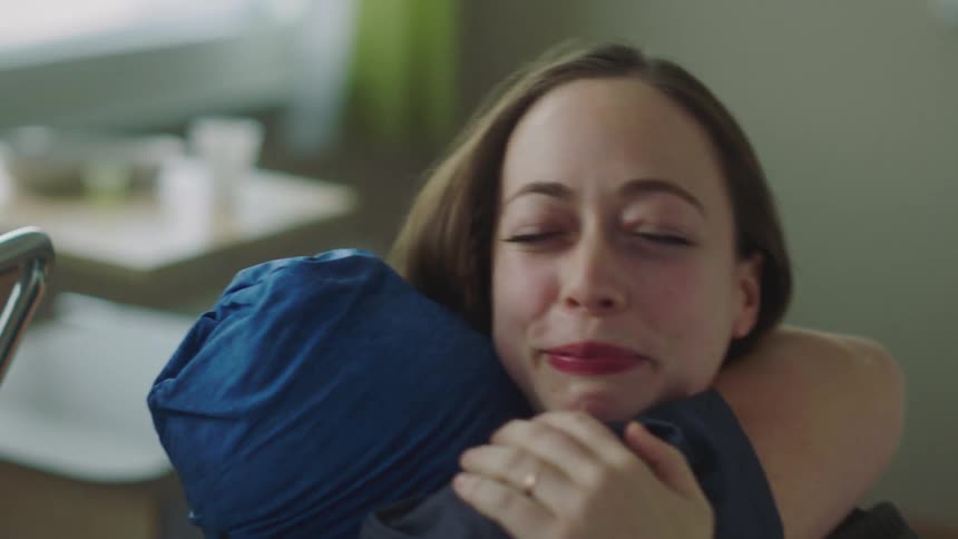 Woman sits near hospital bed listening apprehensively before smiling with relief and hugging hospital patient