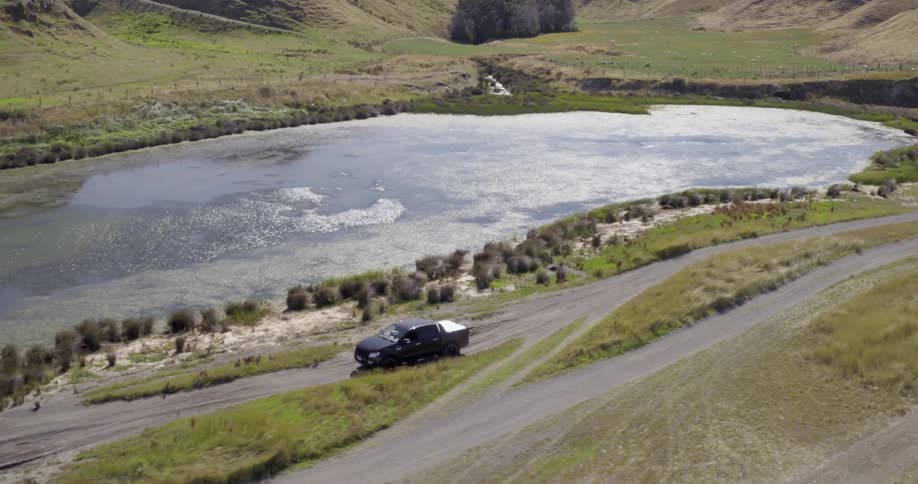 A car drives down a small dirt road by a pond