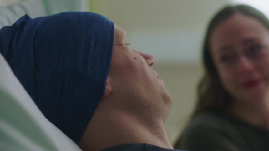 Hospital patient and female relative visiting him both cry before she tries to comfort him