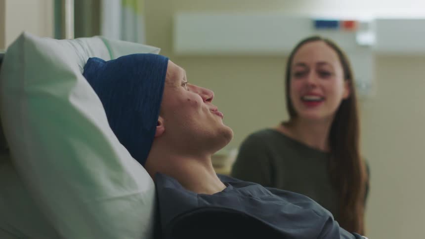 A man lying in a hospital bed talking and laughing with a woman visiting him