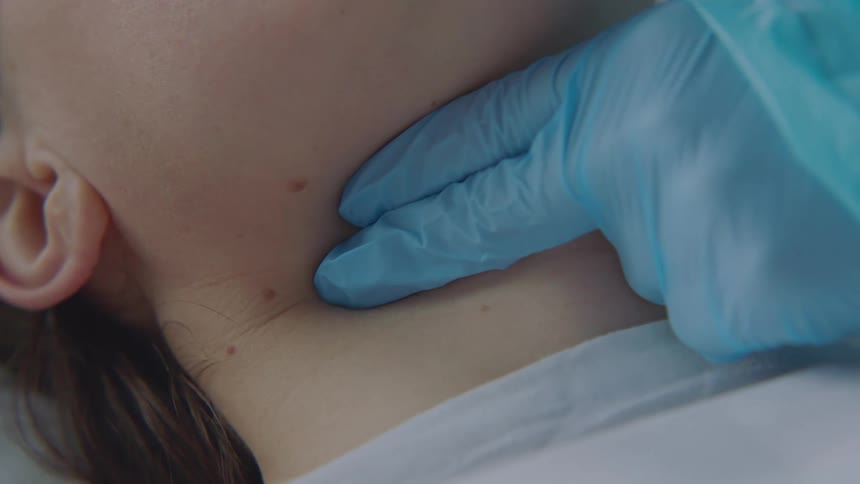 A doctors gloved fingers press down on a patients throat