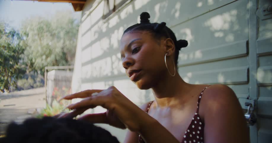A woman sits on a porch braiding hair