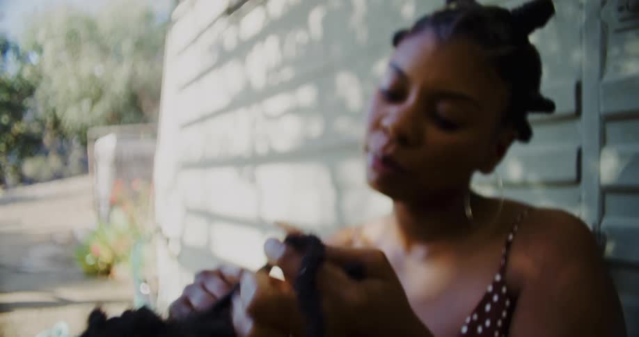 A woman braids a mans hair outside