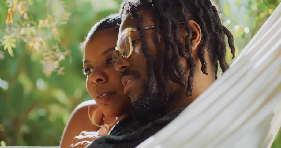 A woman rubs a mans chest as he talks while they lie in a hammock