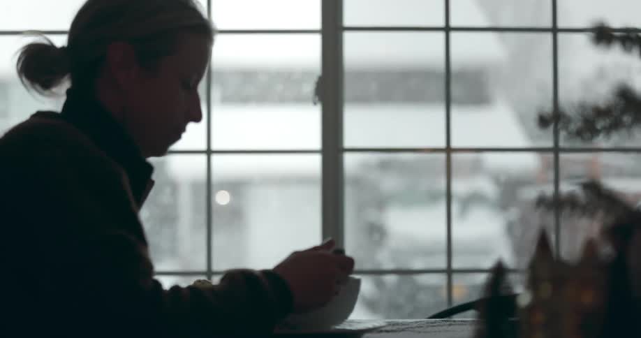 The silhouette of a woman looking out at the snowfall then going back to eating