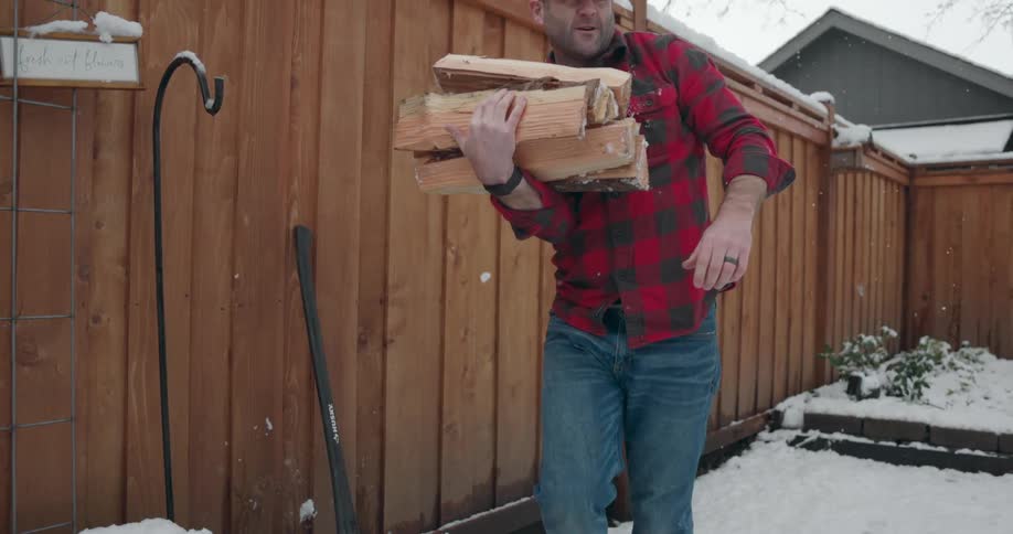 A man is in his backyard and carrying logs of wood