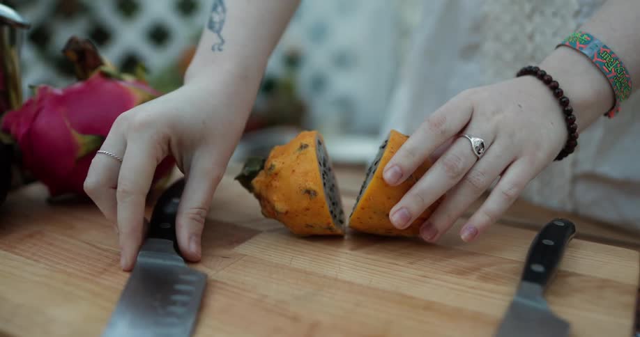Young pale woman cuts a dragon fruit with a sharp kitchen knife