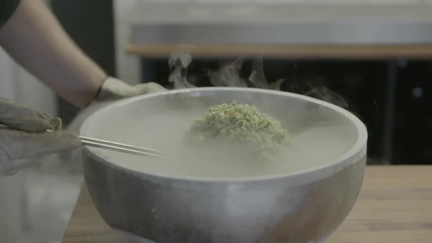 A person is mixing something in a silver bowl with steam coming off it