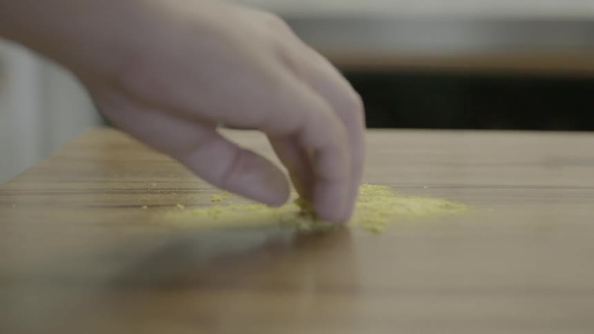 A hand touches a yellow grainy substance on a table top