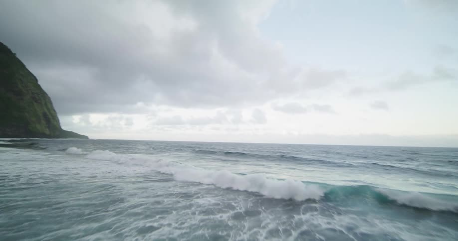 Waves splash and foam as they roll in on the shore under a cloudy sky