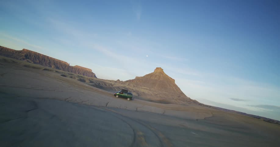 A van travels through the desert badlands among mesa and rock formations