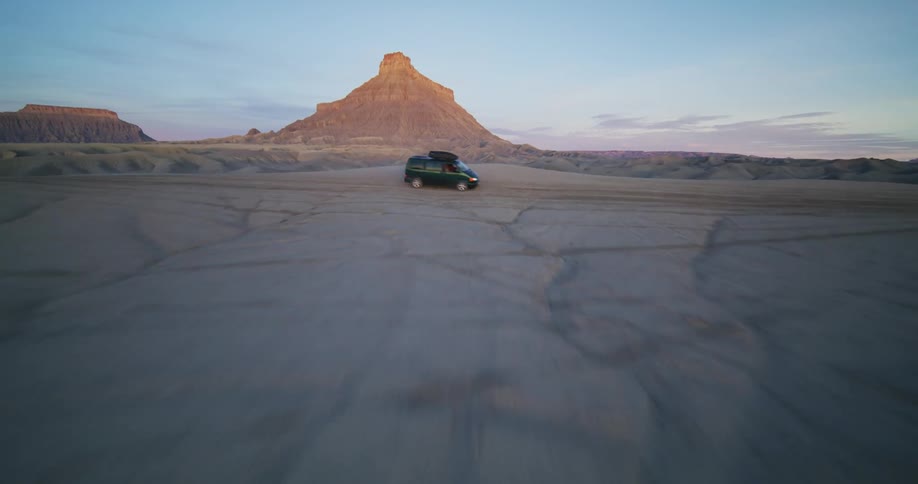 Vehicle rides across desert with plateau and mesa in the background