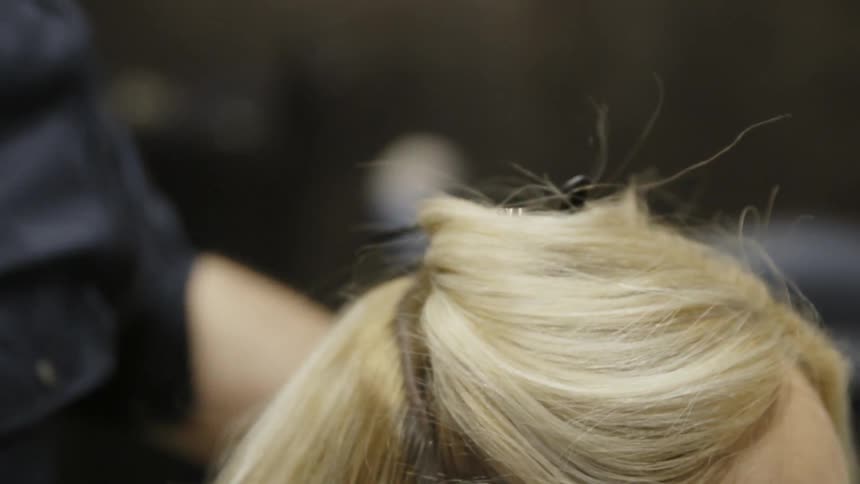 A hair stylist clips up some of a woman's hair
