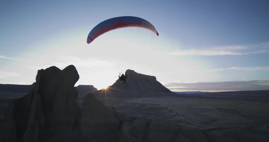 A person parachutes down in towards a desert canyon