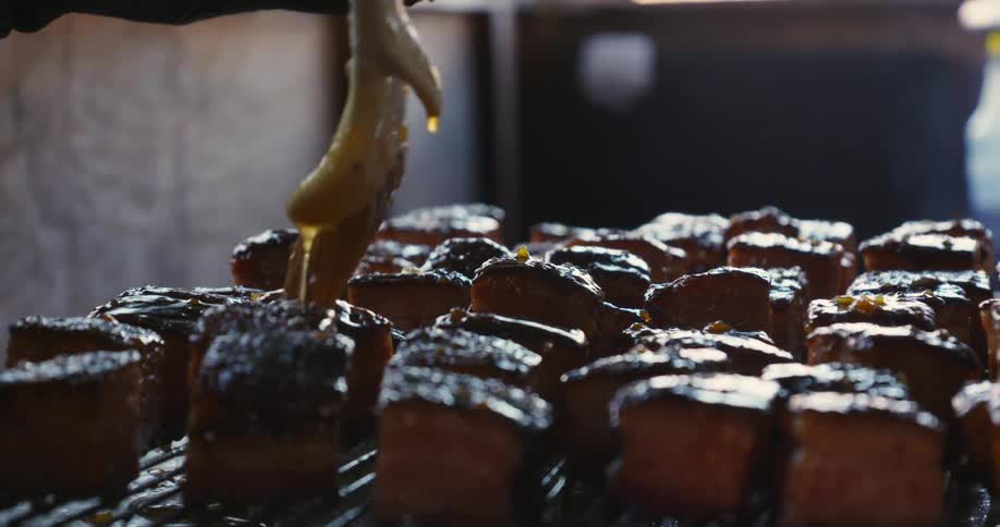 A chef pours honey marinade all over meat on a grill