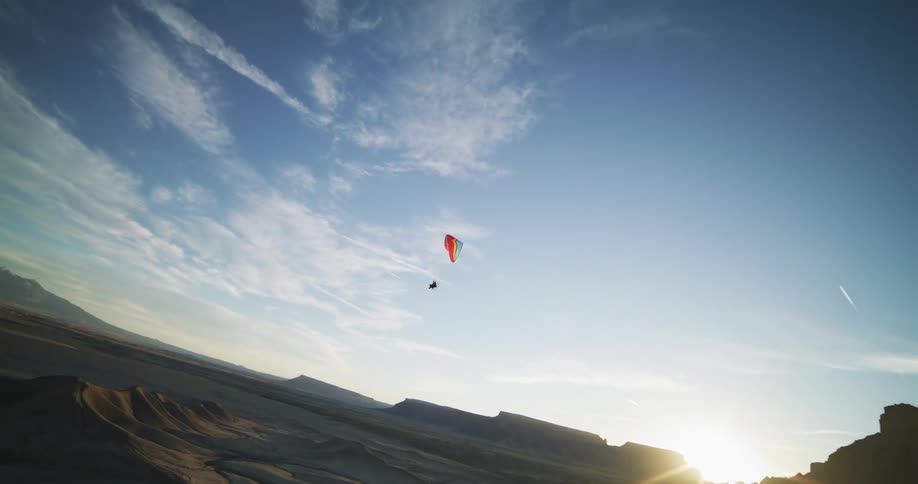 A hang glider floats over the desert dunes and rock formations