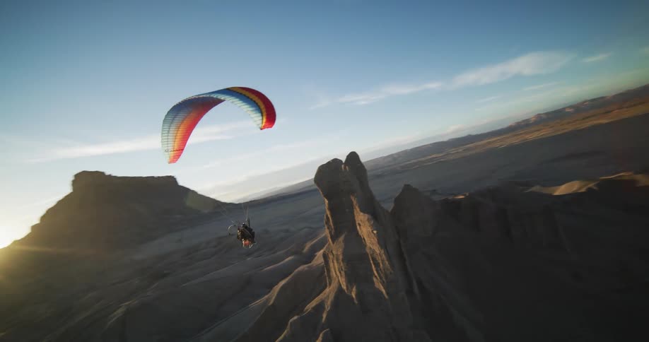 A paraglider flies near a tall mesa in a canyon