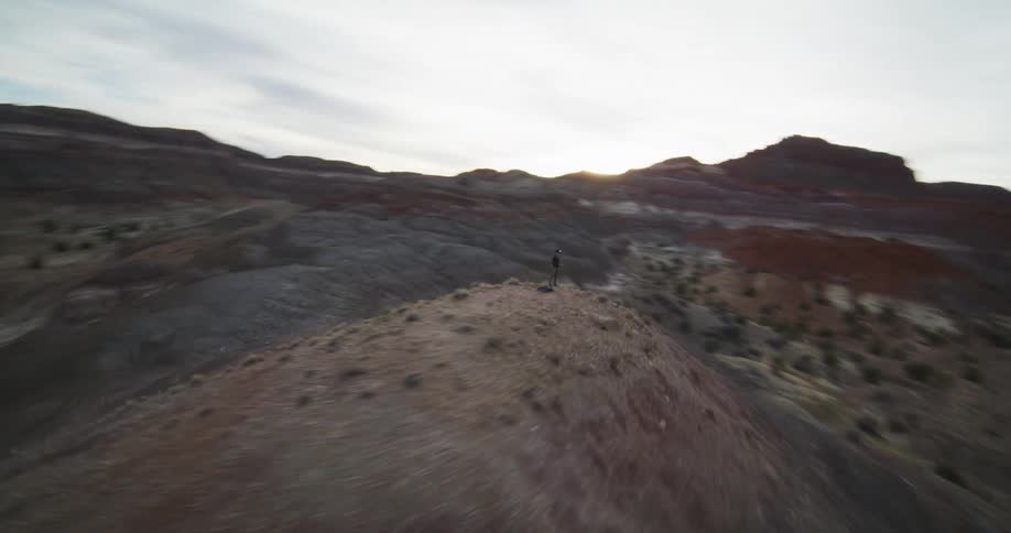 A man stands atop a hill in the desert canyon landscape