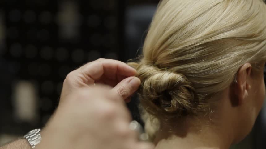 A blonde woman's hair is being tied in a bun