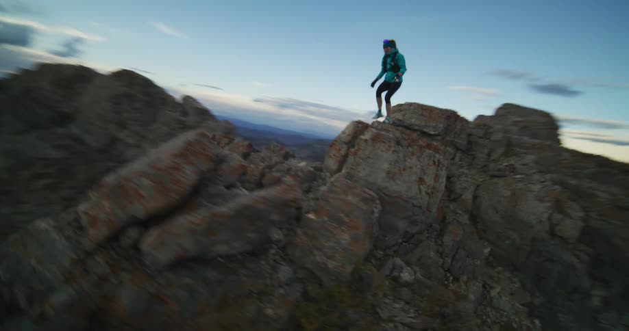 A female hiker jumps down the rocks on a narrow stone cliff above a canyon