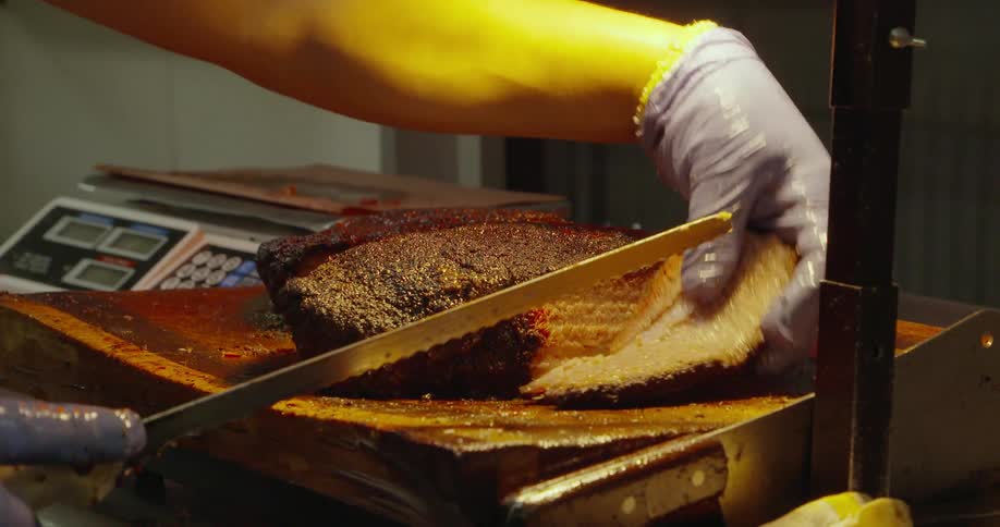A bbq employee cuts off slices of brisket to weigh on a scale