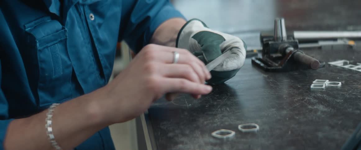 A woman in a shop files a small piece of metal