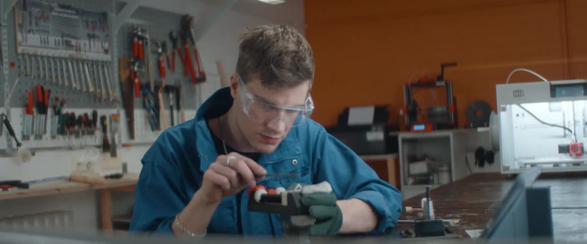 A man files down a small object created with a three dimensional printer