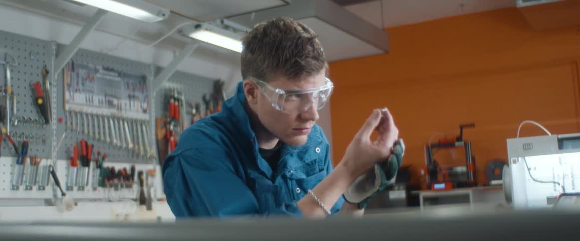 A man sits at a work bench inspecting something closely