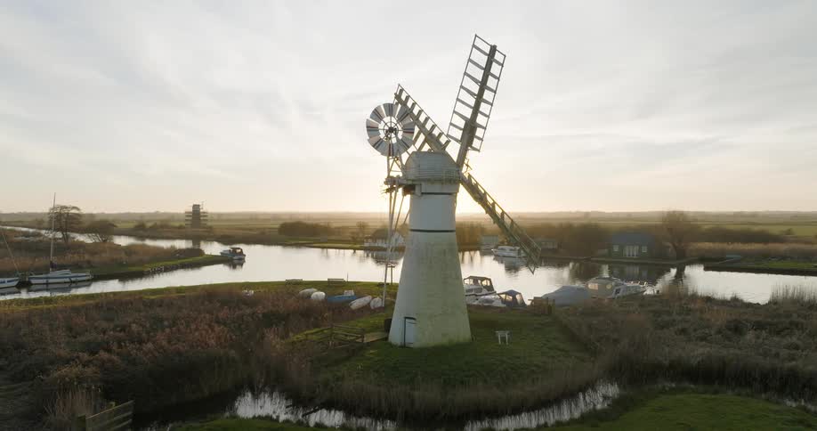 Aerial view of a windmill near a river on the countryside at morning