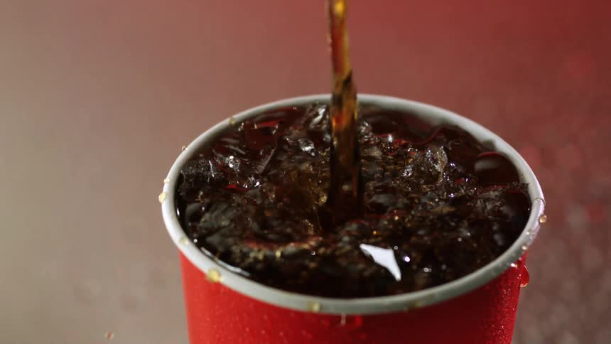 Soda splashes up and out of a red cup as it is poured over ice