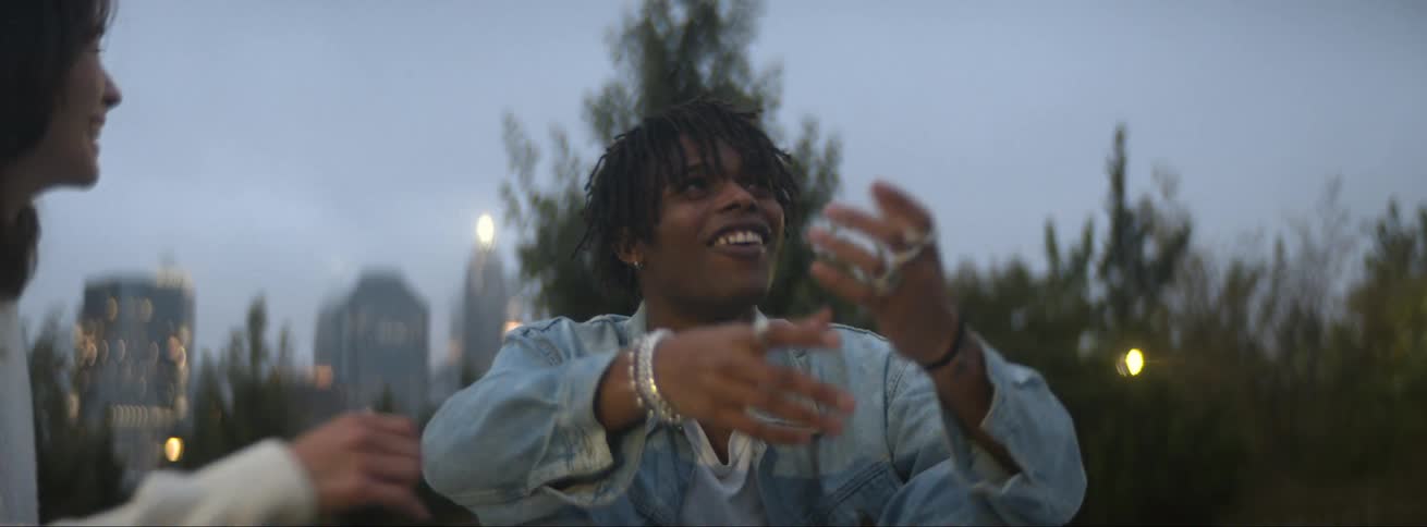 Young couple sitting on the ground in a park laughing and smiling in front of the city skyline