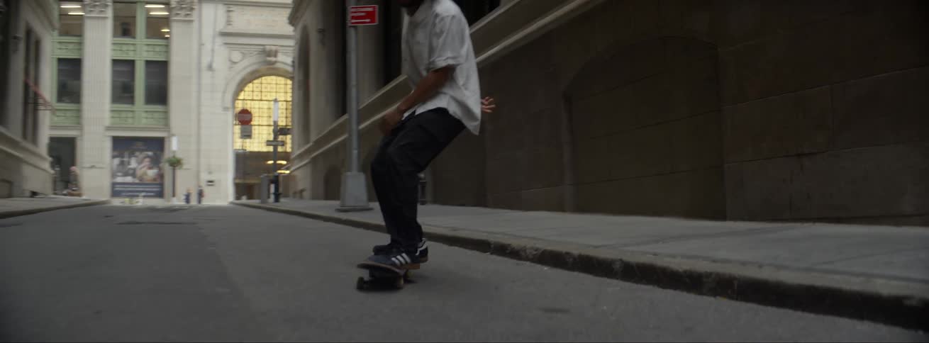 A man jumps off the curb on his skateboard and continues riding down a city street