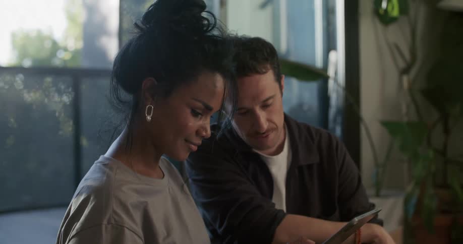 A woman smiles and nods as she looks at a tablet while sitting beside a man