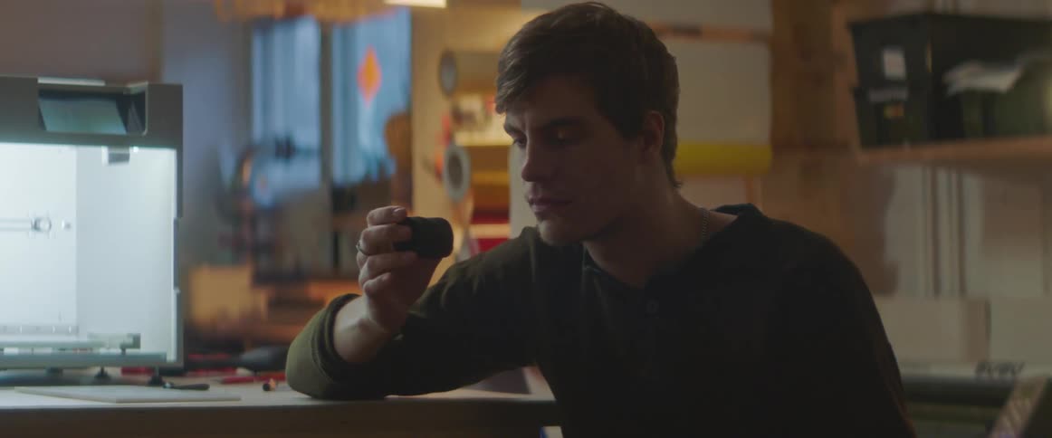 A man sitting holding a small black object in his hand turning it and examining it
